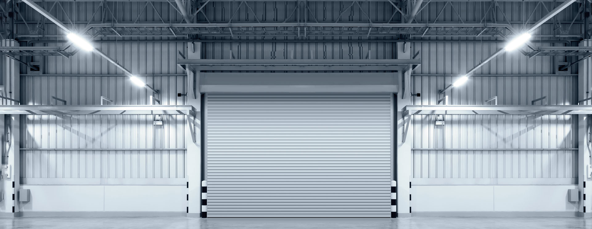 Interior view of an industrial facility featuring a large, closed overhead door with metal framing, surrounded by well-lit structural beams. Designed for Utah businesses seeking secure and efficient commercial garage door solutions.