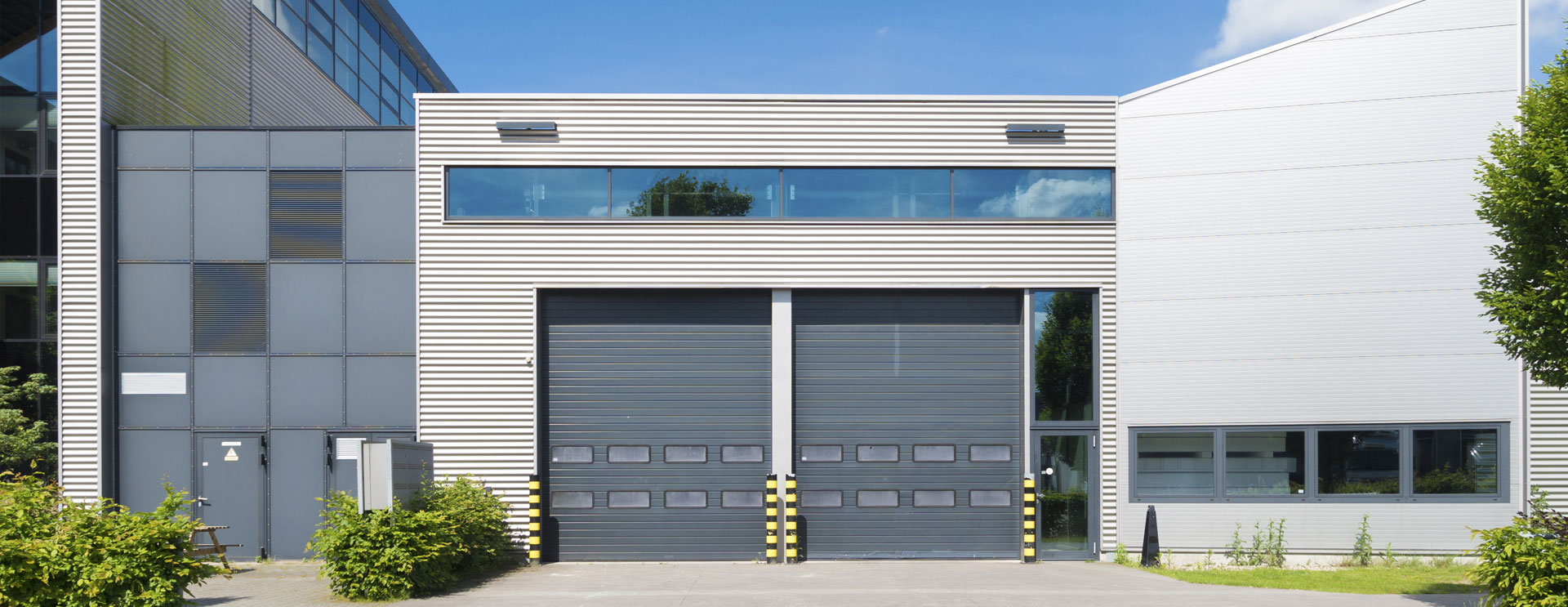 Modern industrial building with two large custom overhead doors and upper windows, featuring a clean architectural design. Ideal for commercial applications in Utah, providing efficient and secure access solutions.
