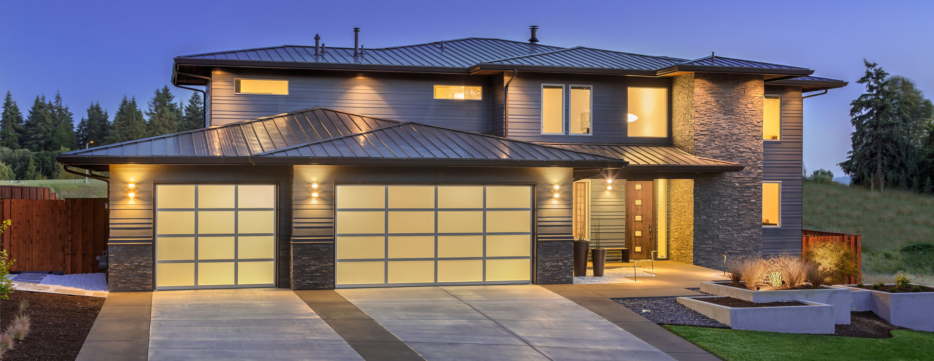 Modern two-story home with illuminated glass-panel garage doors, enhancing curb appeal and providing a contemporary aesthetic. Perfect for Utah homeowners seeking stylish, high-quality garage door solutions.